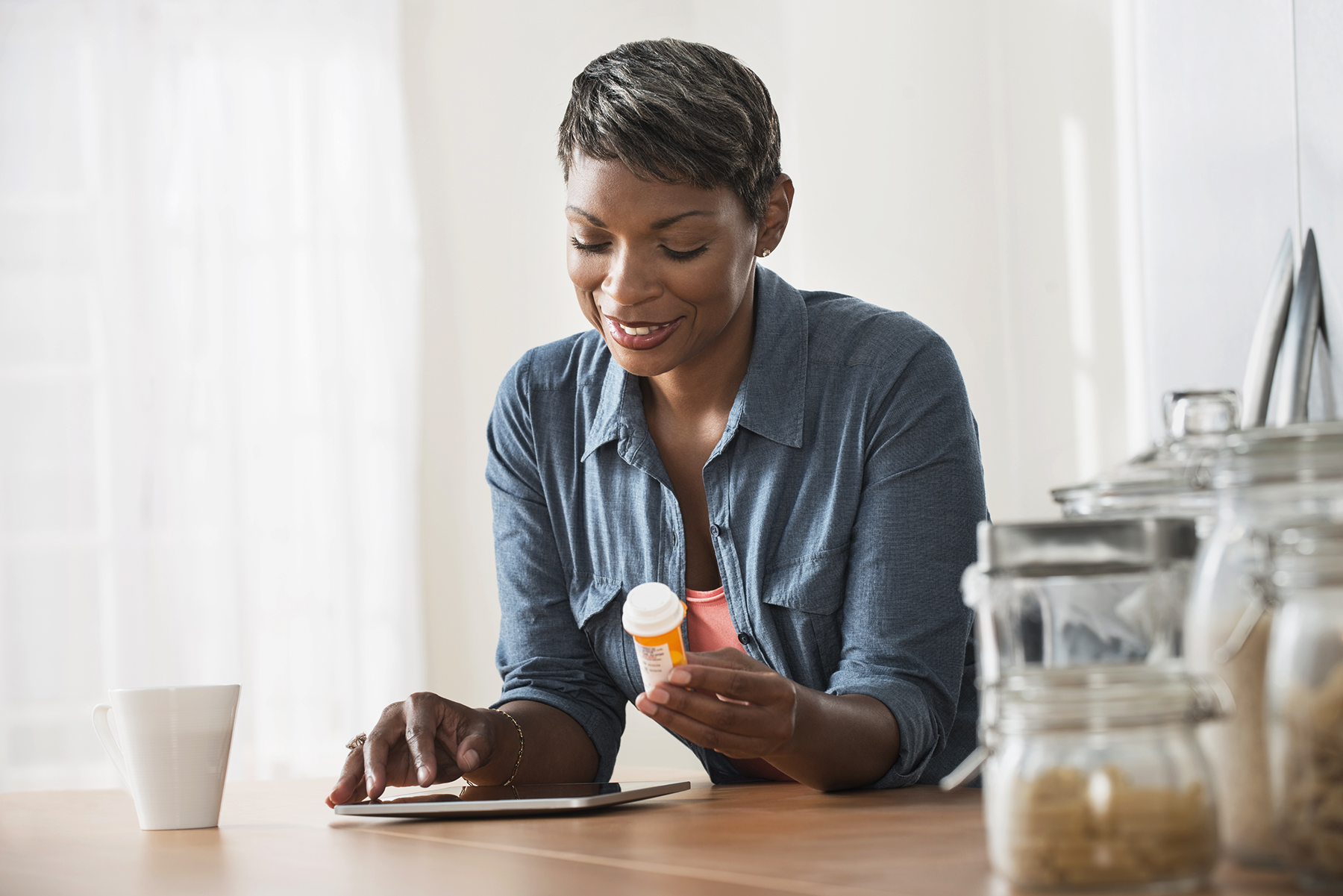A woman holds a prescription bottle while leaning over a table.