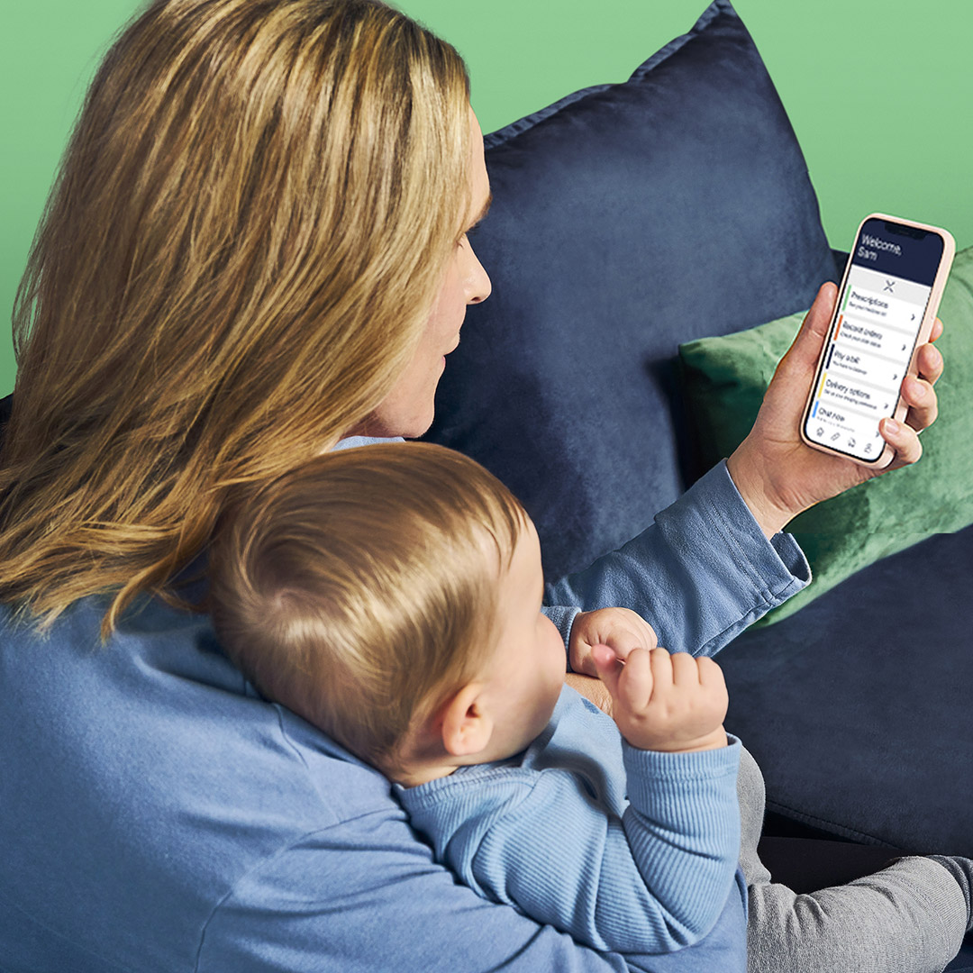 A woman uses the Express Scripts® Pharmacy app on her mobile phone while sitting with her baby on her lap.