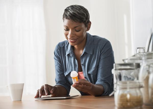 A woman holds a prescription bottle while leaning over a table.