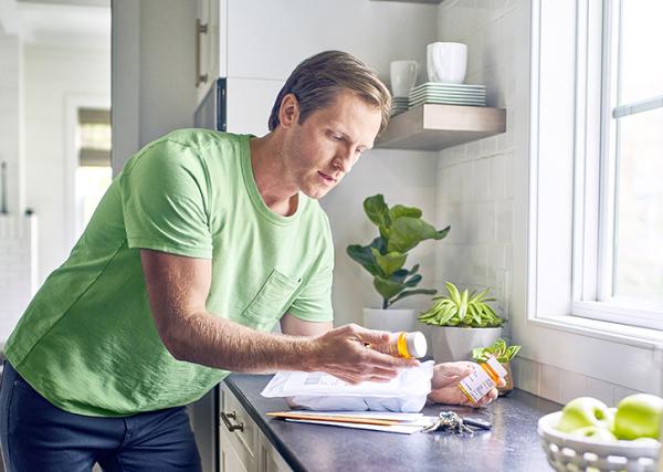 A man leans over a counter while holding two prescription bottles.