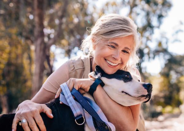 An older woman hugs her dog while taking a walk outside.