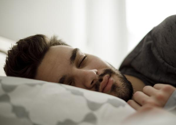 A man sleeps peacefully in his bed as the morning sunlight comes through