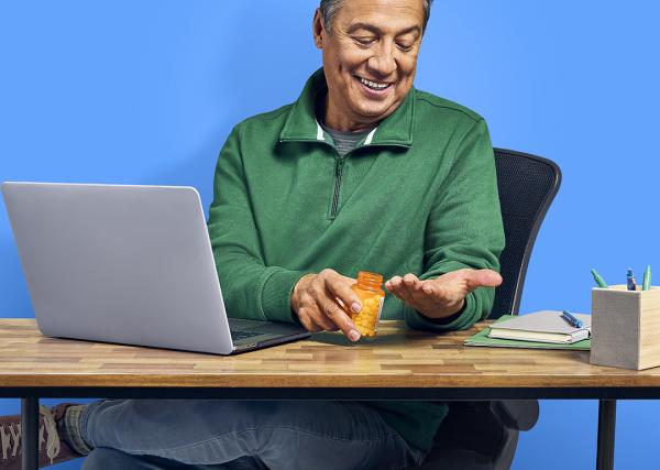 A man holds a prescription bottle for a maintenance medication while looking at the medication in his other hand.