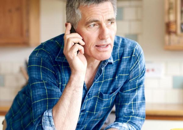 A man talks to a pharmacist on his phone from his kitchen.