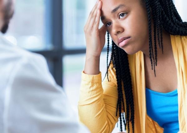 A stressed teenage girl puts her hand to her forehead as she sits with her pediatrician.