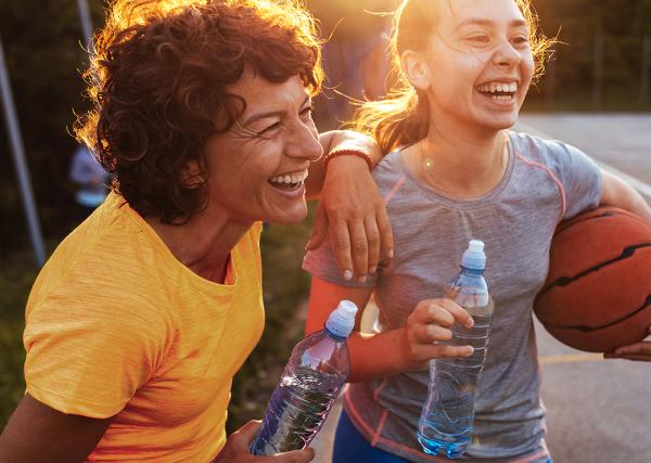 A woman enjoys a water break with her teen daughter and son during a casual basketball game.