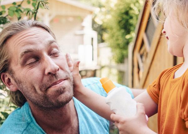 A young girl applies sunscreen to her father’s face.