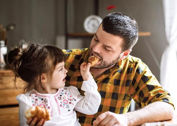 A toddler feeds her father a piece of her croissant.