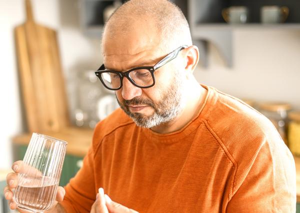 A man holds a glass of water in one hand and a pill in the other.