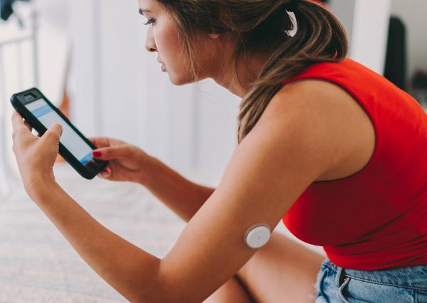 A young woman using a continuous glucose meter checks her blood sugar on an app.