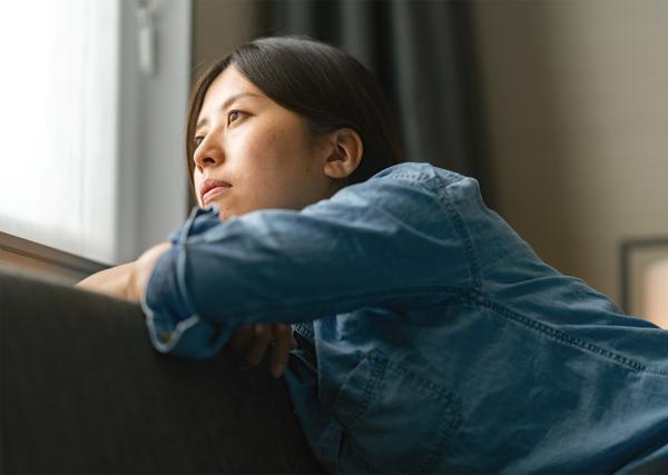 A young woman inside her home looks out her window longingly.