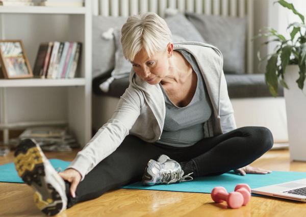 An older woman stretches on a mat on the floor of her home.