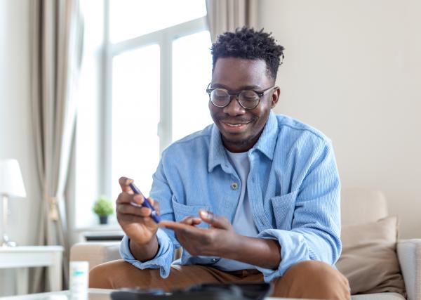 A young man checks his blood sugar while sitting on the couch.