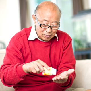 An older man empties a pill into his hand from a medication bottle.