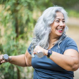 A woman exercises outdoors while holding a set of dumbbells.