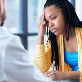 A stressed teenage girl puts her hand to her forehead as she sits with her pediatrician.