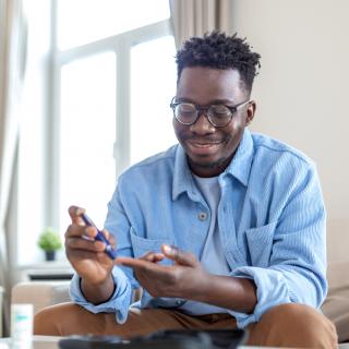 A young man checks his blood sugar while sitting on the couch.